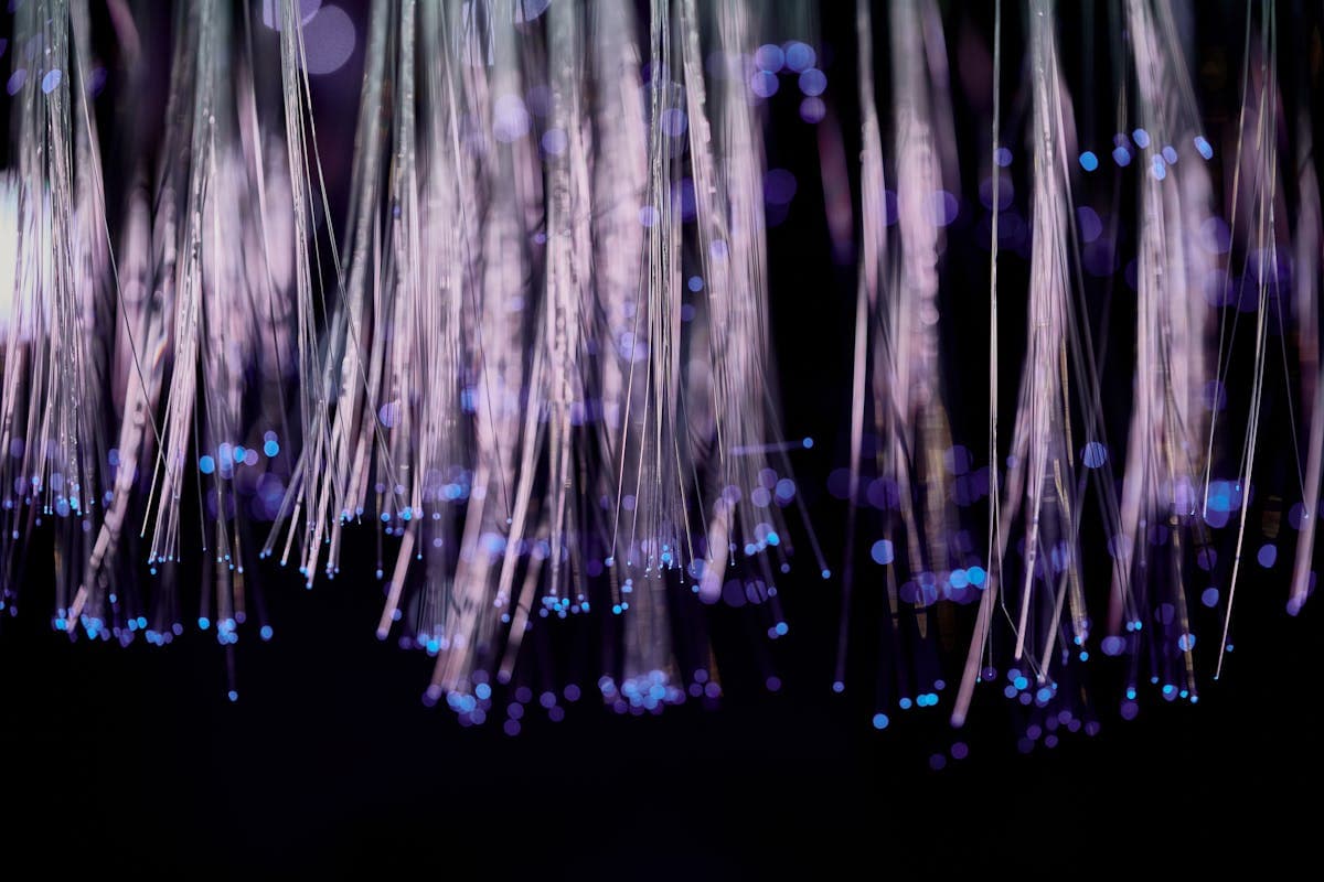 Fibras ópticas iluminadas con efecto bokeh en tonos azules y violetas que contrasta visualmente con la transmisión de un solo modo en la fibra monomodo, ilustrando la diferencia fundamental entre ambos tipos de fibra óptica